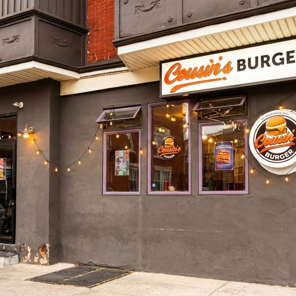 Exterior of Cousin's Burger restaurant with a gray facade, string lights, and prominent signage.