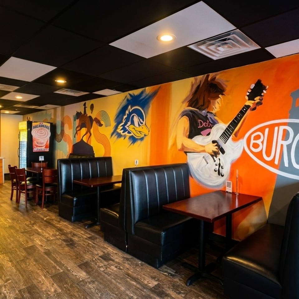 Restaurant interior with colorful murals, black booths, wooden tables, and a person at the counter.
